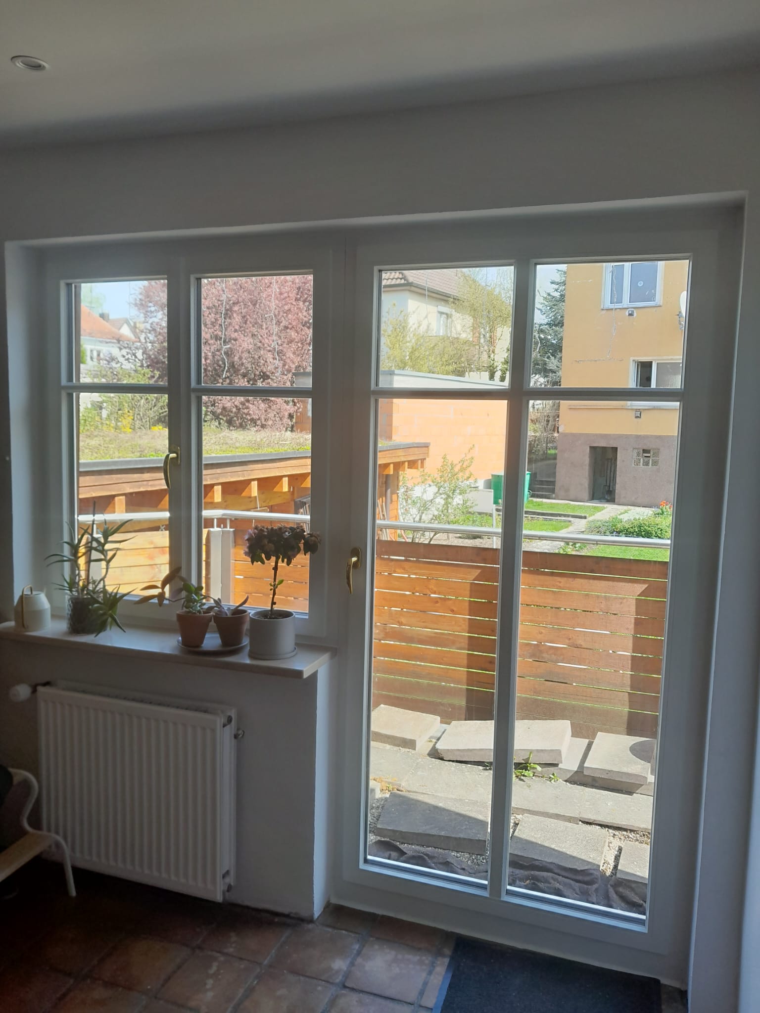 Sonnenlicht fällt durch ein großes Fenster auf Pflanzen und einen hellen Holzzaun