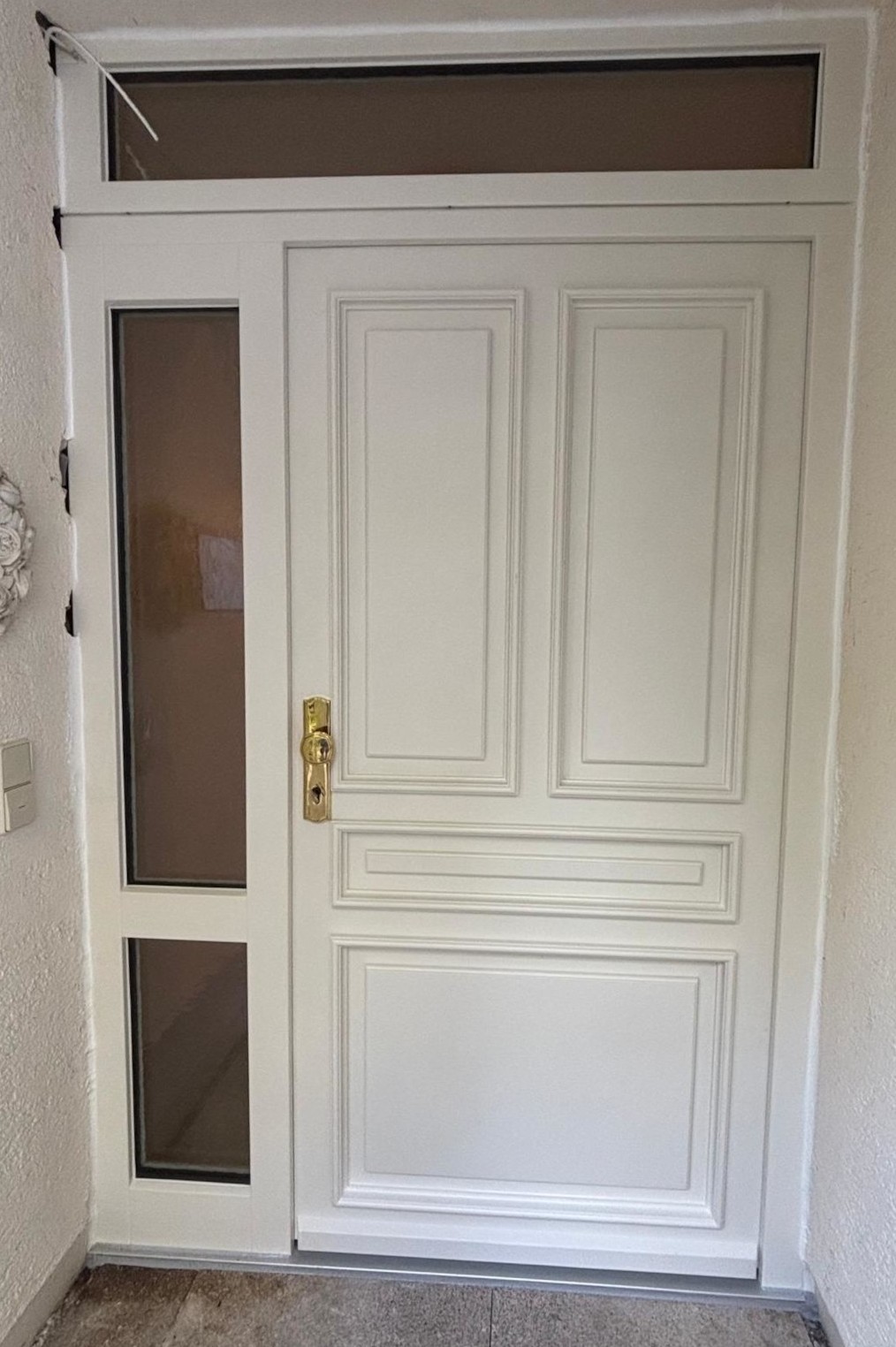 Weiße Haustür mit Glaseinsätzen und goldener Klinke in schlichtem Eingangsbereich