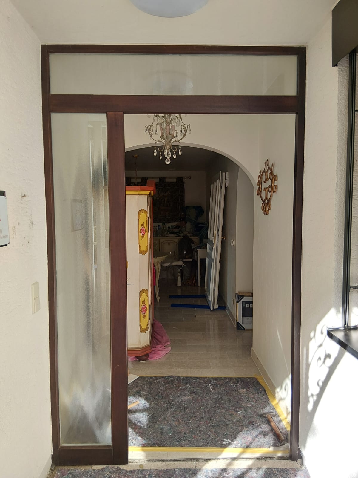 Ein heller Flur mit Glastür, im Hintergrund bemalter Schrank und Kronleuchter